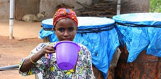 One of Abdullah’s daughters takes a drink of water from a clay water storage jar. The donkey cart and drums used for transporting water to the house stand behind her.