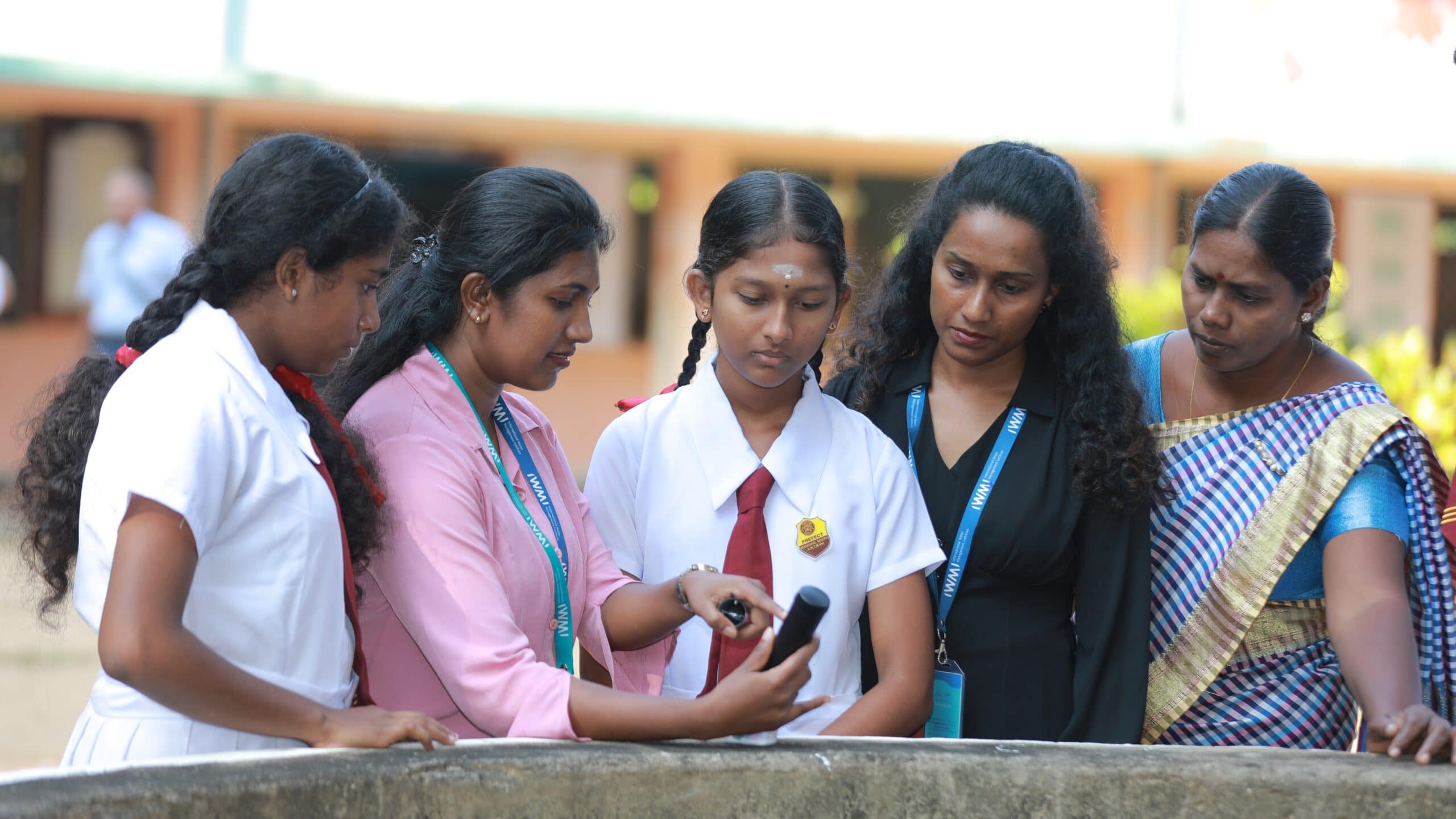 At a school in Chavakachcheri, IWMI researchers Dilmi Sithara Gamage, second from left, and Suvasthigha Puvanenthirarajah, fourth from left, demonstrate how to use an electric conductivity meter to student citizen scientists and a teacher. Photo: IWMI