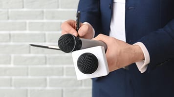 journalist with microphones on brick background. Photo: Pixel-Shot/Shutterstock