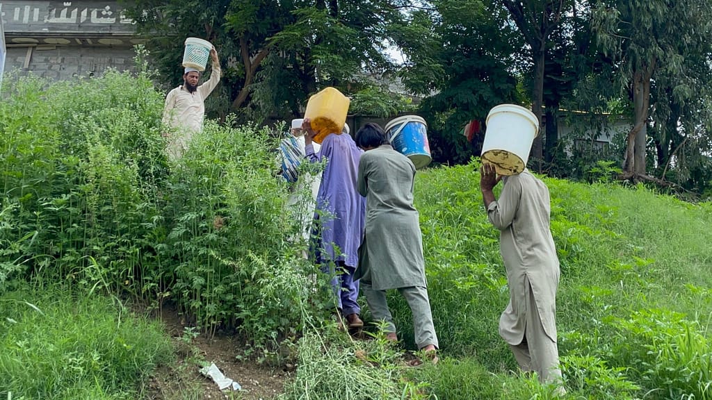 A group of villagers carry buckets filled with water from the downstream source, navigating steep terrain to bring water back to their homes. Photo: Naqash Abbasil/IWMI