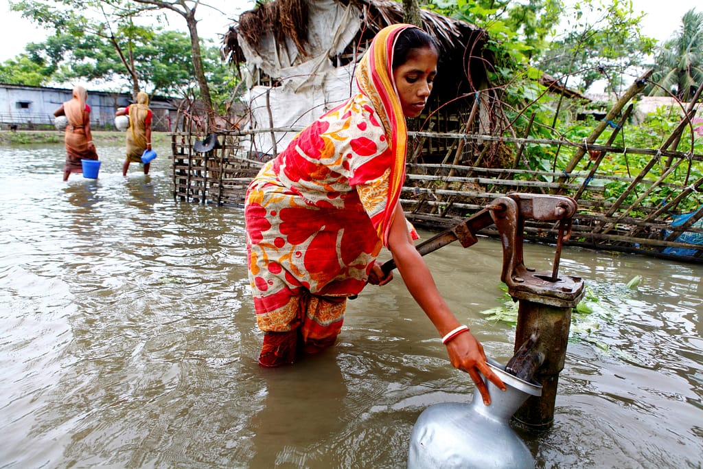 A woman paumps water from a well while standing knee-deep in floodwaters that have inundated the Satkhira district in southwestern Bangladesh. Photo: G.M.B. Akash/Panos Pictures