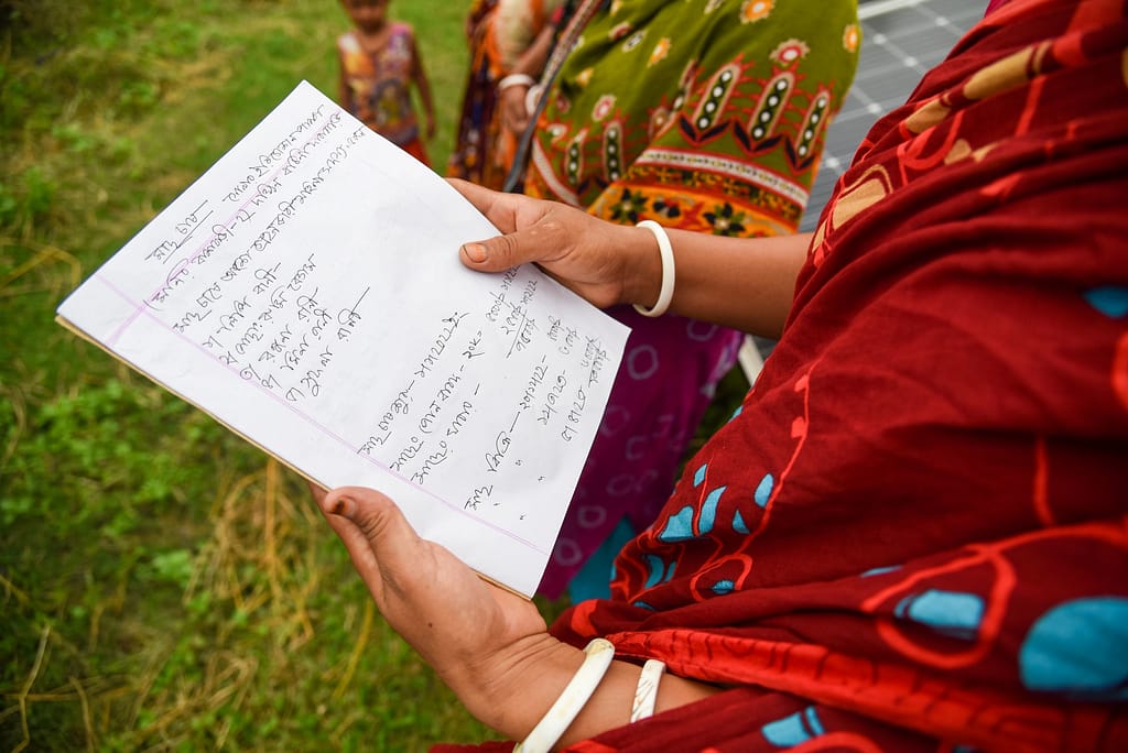 Lipi Rani, 35, a member of a women’s group engaged in fisheries, displays their book of accounts beneath a solar panel system installed by Infrastructure Development Company Limited (IDCOL) in Thakurgaon on June 9, 2024. With Solar Irrigation Pumps (SIPs) reducing labor in agriculture, women like her have been able to diversify their livelihoods through fish farming. Photo: Tanmoy Bhaduri/IWMI