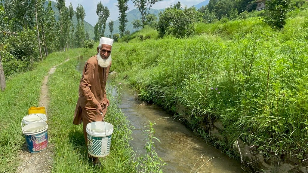 Prior to the installation of hydra ram pump, Akbar Jan carries a bucket of water from the stream, reflecting the difficult journeys villagers once made several times a day to meet basic water needs. Photo: Amjad Jamal/IWMI