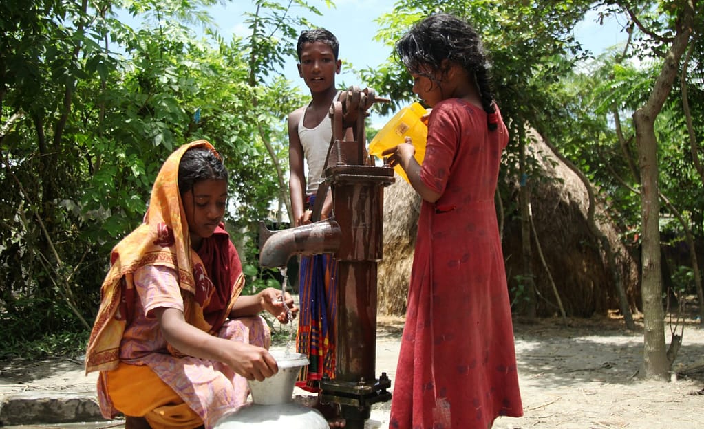 Isolated from the mainland, children at a shelter in Raisaheb Char, and island in Bangladesh, pour water from a jug to mimic flow from tube wells that no longer function. Photo: MA Bashar/Shutterstock