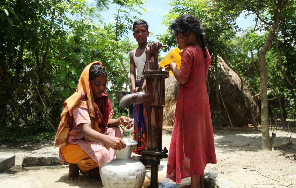 Isolated from the mainland, children at a shelter in Raisaheb Char, and island in Bangladesh, pour water from a jug to mimic flow from tube wells that no longer function. Photo: MA Bashar/Shutterstock