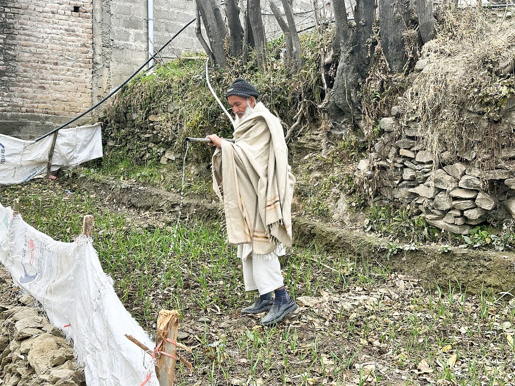An elderly man waters his kitchen garden using surplus water from the elevated storage tank. The system channels excess water downhill through gravity-fed pipes, ensuring no water is wasted while supporting small-scale agriculture. Photo: Amjad Jamal/IWMI